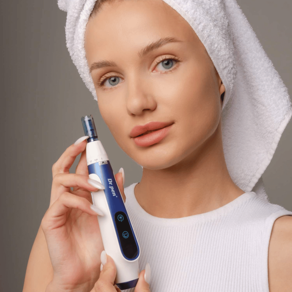 Vrouw met handdoek om haar haar houdt een Dr. Pen A11 microneedling-pen vast – een professioneel huidverzorgingsapparaat voor een gladdere en stevigere huid.